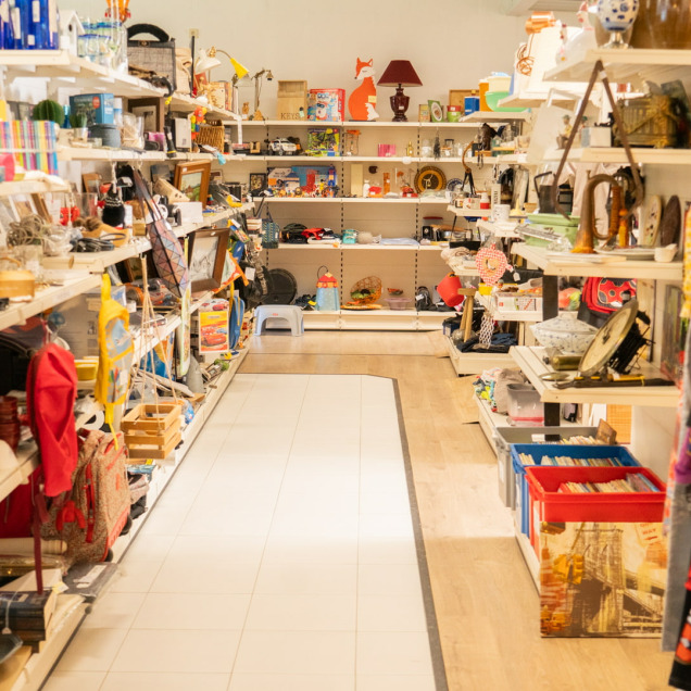 Intérieur du magasin de seconde main Boutique & Brocante à Ouffet, avec des étagères remplies de divers articles de décoration, vêtements et objets d'occasion.