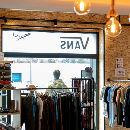 Intérieur du magasin “Bubba Ride” à Liège, avec des vêtements et accessoires exposés sur des portants et des étagères. Un design moderne avec des ampoules suspendues et un mur en bois en arrière-plan