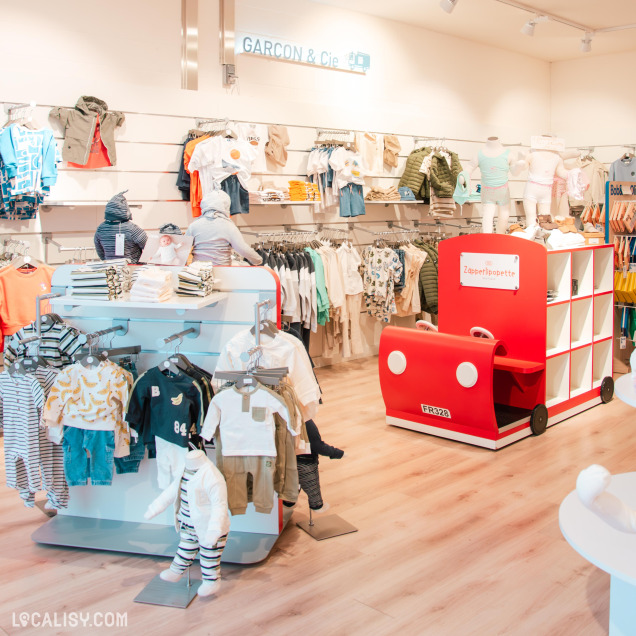 Intérieur du magasin Zapperlipopette, section "Garçon & Cie" avec une grande variété de vêtements pour garçons, organisés sur des portants et des étagères. Un présentoir rouge en forme de voiture ajoute une touche ludique à l’espace.