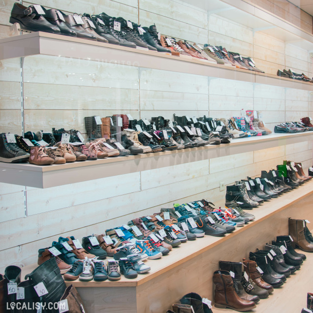 Présentation d’une large sélection de chaussures sur des étagères en bois clair, comprenant baskets, bottines et chaussures pour enfants et adultes, soigneusement alignées.