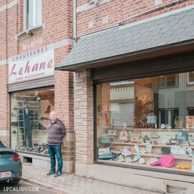 Une vitrine de magasin de chaussures et maroquinerie mettant en avant des sacs à main, des baskets et des accessoires aux tons pastel et métallisés. Les articles sont soigneusement disposés sur des étagères en marbre beige.