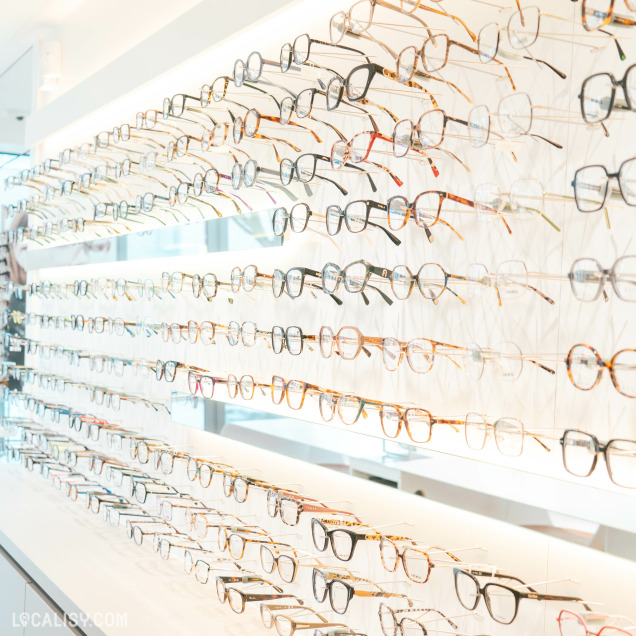 Présentation soignée d’une large sélection de lunettes de vue, suspendues sur une paroi lumineuse. Les montures sont variées en couleurs et en styles, allant du classique au plus tendance.