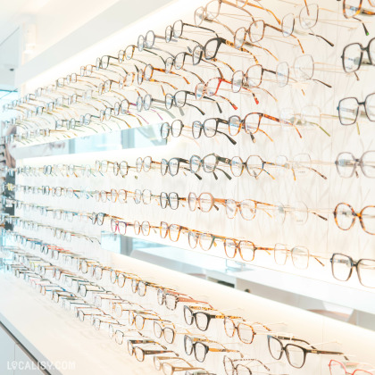 Présentation soignée d’une large sélection de lunettes de vue, suspendues sur une paroi lumineuse. Les montures sont variées en couleurs et en styles, allant du classique au plus tendance.