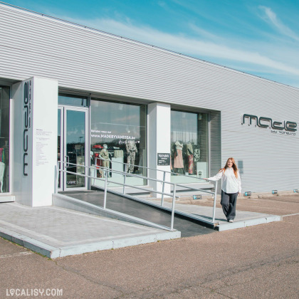 Façade du magasin Made by Vanessa à Huy, avec une rampe d’accès et une vitrine lumineuse mettant en avant des vêtements tendance.
