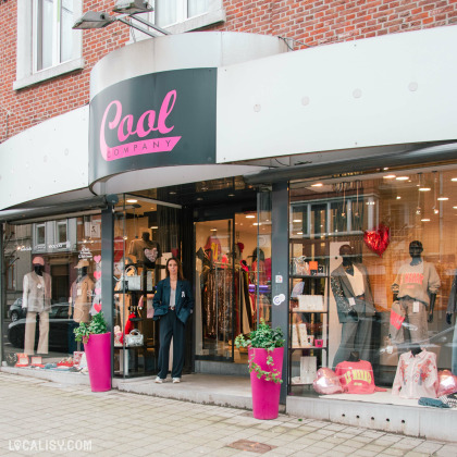 Façade de la boutique Cool Company, une enseigne de prêt-à-porter tendance. Devanture vitrée avec mannequins en vitrine et une femme accueillante à l’entrée. Ambiance chaleureuse et invitation à découvrir la mode en boutique.