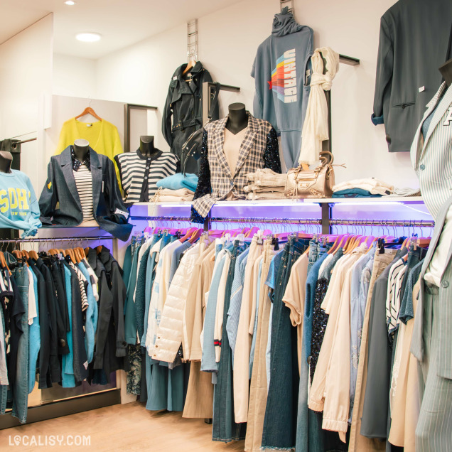 Présentation de vêtements bleu marine, beige et denim dans une boutique de mode. Vestes, manteaux et accessoires élégants exposés sur des mannequins et des portants. Éclairage moderne et mise en valeur des collections.