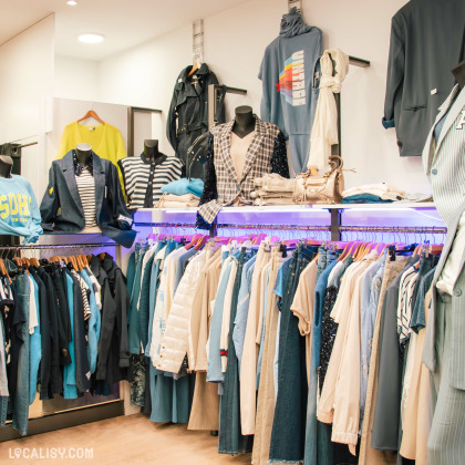 Présentation de vêtements bleu marine, beige et denim dans une boutique de mode. Vestes, manteaux et accessoires élégants exposés sur des mannequins et des portants. Éclairage moderne et mise en valeur des collections.
