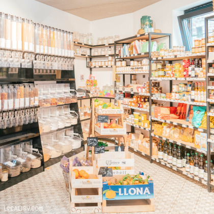 Un coin de l’épicerie dédié aux produits en vrac avec des distributeurs de céréales, de noix et de légumineuses. Les étagères en métal noir accueillent une grande variété de produits locaux : confitures, huiles, biscuits et condiments. Des cagettes en bois remplies de fruits frais complètent cet espace écoresponsable et gourmand.