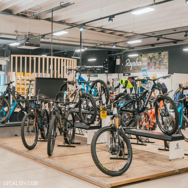 Une section mettant en avant des VTT suspendus et exposés sur des supports pour faciliter leur visibilité. Des modèles aux cadres robustes et aux pneus larges témoignent d’une offre adaptée aux amateurs de sensations fortes. Le décor moderne et organisé du magasin met en valeur chaque catégorie de vélos.