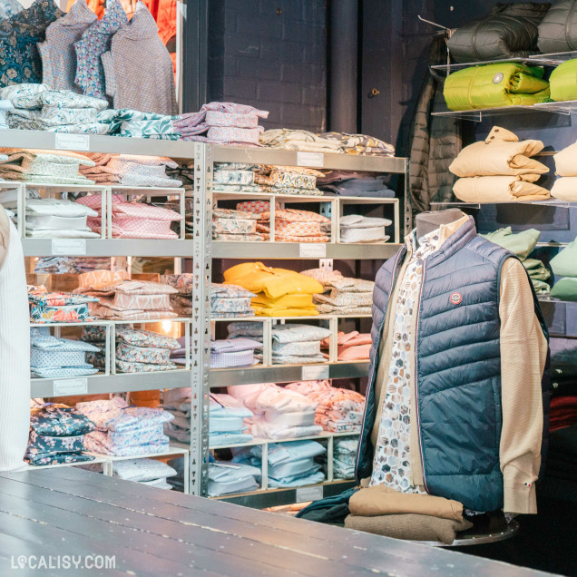 Présentoir de vestes et chemises aux couleurs vives dans le magasin Ce que veulent les hommes à Huy.