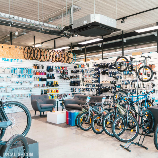 Rayon accessoires du Bicyclic Bike Shop Remouchamps, avec des roues suspendues, des pièces détachées Shimano, des équipements de cyclisme colorés, ainsi qu’un coin détente avec fauteuils et canapés.