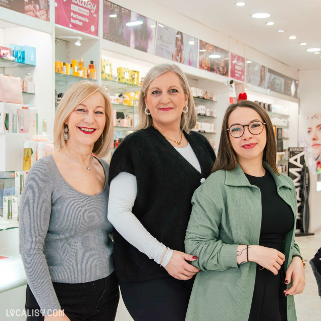 Équipe souriante de trois femmes travaillant dans le magasin de parfum Audrey à Fléron, posant devant les rayons de produits de beauté.