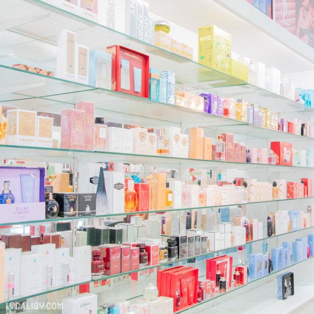 Rayons garnis de parfums de grandes marques dans le magasin de parfum Audrey à Fléron, avec des étagères en verre bien éclairées et colorées.