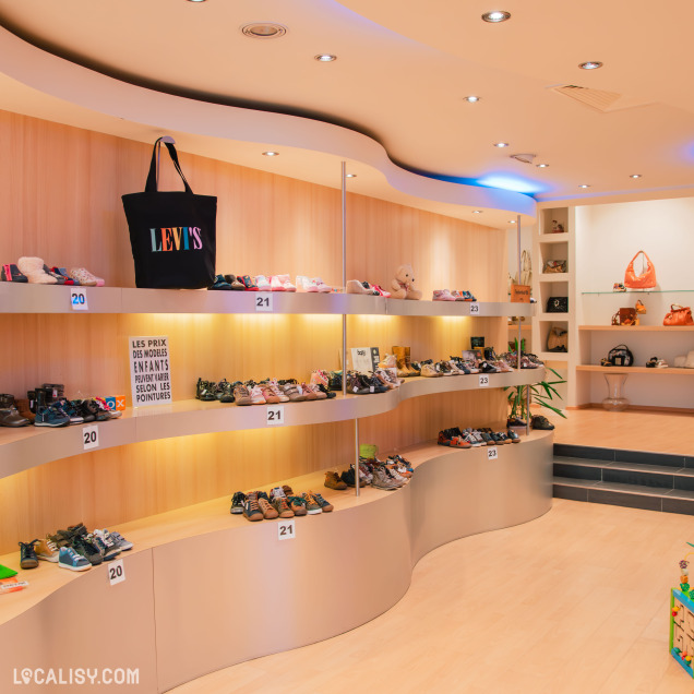 Rayon enfants du magasin de chaussures à Aywaille avec des paires classées par pointure sur des étagères ondulées, et un décor chaleureux en bois clair.