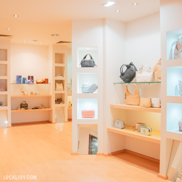 Intérieur lumineux et moderne d'un magasin de sacs à main à Aywaille, avec des étagères murales blanches mettant en valeur différents modèles de sacs.