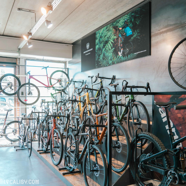 Espace showroom du magasin DC Team Bike dédié aux vélos de gravel et de route, alignés sur un présentoir en bois avec une affiche murale mettant en scène un cycliste en pleine nature.