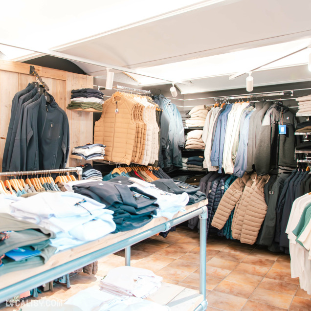 Rayon de vestes, gilets matelassés et sweats pliés sur étagères dans un espace bien organisé au sol carrelé, typique d’un magasin de vêtements haut de gamme.