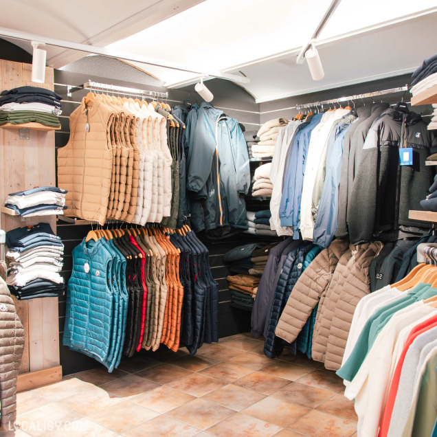 Vue détaillée d’un coin du magasin avec des gilets sans manches de différentes couleurs suspendus à côté de vestes et sweats soigneusement rangés.