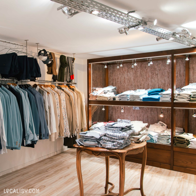 Espace chic du magasin avec chemises, vestes habillées et pulls soigneusement pliés sur des étagères en bois, ambiance chaleureuse et raffinée.