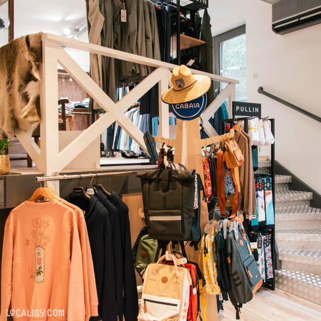 Vue intérieure d'une boutique de vêtements, avec une sélection de sacs à dos, vêtements de sport et accessoires de la marque Cabaïa, affichés de manière soignée sur plusieurs étagères et portants.