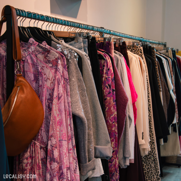 Zoom sur des vêtements texturés et colorés : robe fluide à motifs rose-violet, pull gris à sequins, et diverses pièces féminines élégantes suspendues en boutique.