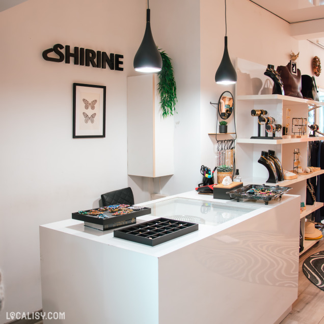 Comptoir élégant d’une boutique de bijoux et accessoires, avec éclairage suspendu, présentoirs de bijoux colorés et décoration soignée. Le nom “Shirine” est visible sur le mur