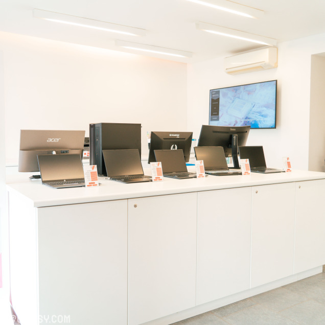 Comptoir de présentation avec plusieurs ordinateurs portables et fixes exposés dans un magasin informatique lumineux et moderne.