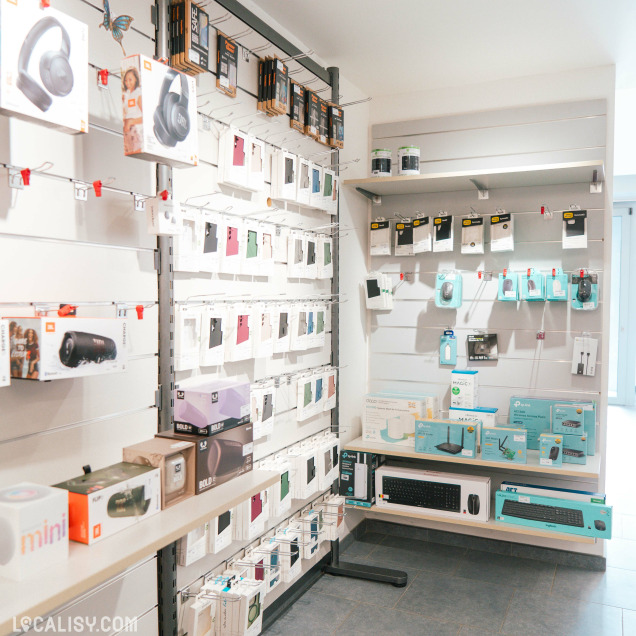 Rayon d’accessoires informatiques avec écouteurs, coques de téléphone, enceintes portables et autres produits tech suspendus ou rangés sur étagères.