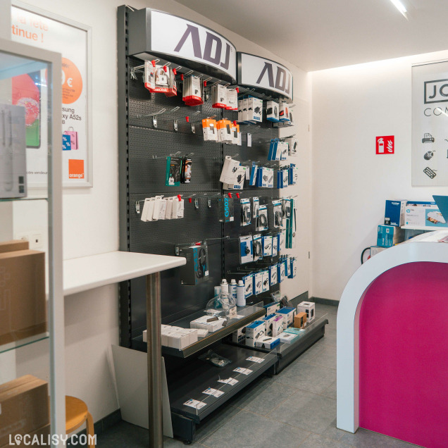Espace de vente avec des accessoires informatiques suspendus sur un panneau noir, sous une enseigne ADJ, dans un coin du magasin.