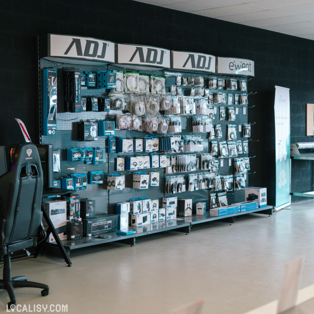 Rayon accessoires avec des produits de la marque ADJ et Ewient : câbles, claviers, souris, casques, hubs USB et autres équipements, soigneusement rangés sur un mur perforé noir.
