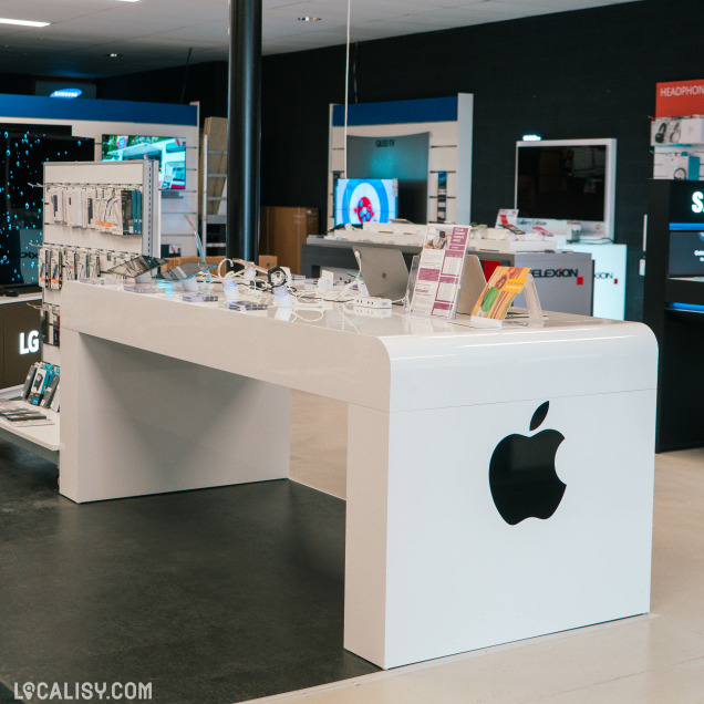 Table de présentation Apple dans un magasin high-tech, avec des accessoires, des montres connectées et des ordinateurs portables en exposition. Le logo Apple est bien visible sur le mobilier blanc.