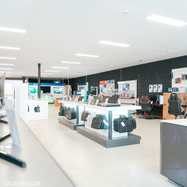 Aperçu large de l’agencement du magasin avec des comptoirs d’ordinateurs portables, le mobilier Apple reconnaissable à son logo, et un espace gaming à l’arrière-plan.