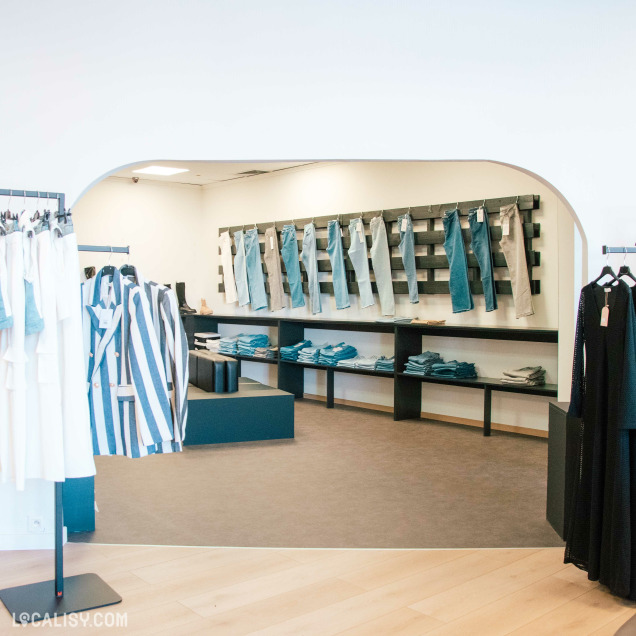 Magasin de vêtements Other Side à Amay mettant en valeur un mur de jeans et une gamme de vêtements en denim.