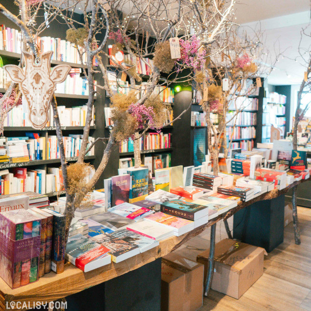 Vue intérieure de la librairie Livre'S à Marche-en-Famenne avec une table de livres sous une décoration végétale.