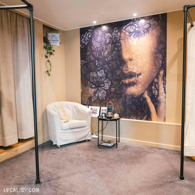 Cabine d'essayage du magasin de lingerie La pince à Linge à Wanze avec un fauteuil et une décoration murale.