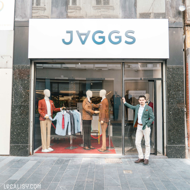 Façade du magasin de costumes sur mesure Jaggs à Liège, avec un homme posant devant la vitrine.