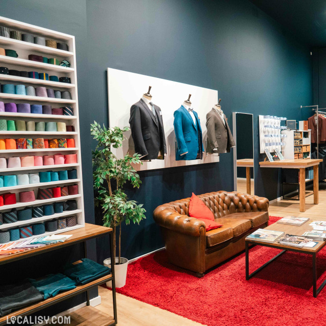 Intérieur du magasin de costumes sur mesure Jaggs à Liège, avec un canapé en cuir et des mannequins.