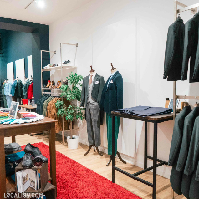 Vue d'ensemble de l'intérieur du magasin de costumes sur mesure Jaggs à Liège, avec des mannequins et des articles.
