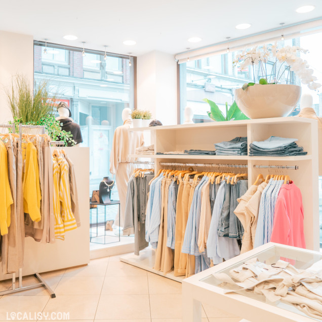 Ambiance intérieure de la Boutique Georgette à Huy avec des vêtements clairs et colorés.