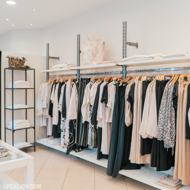 Assortiment de vêtements neutres et noirs sur des portants dans la Boutique Georgette à Huy.