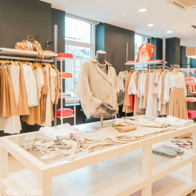 Intérieur de la Boutique Georgette à Huy, présentant des vêtements sur des étagères et des portants.