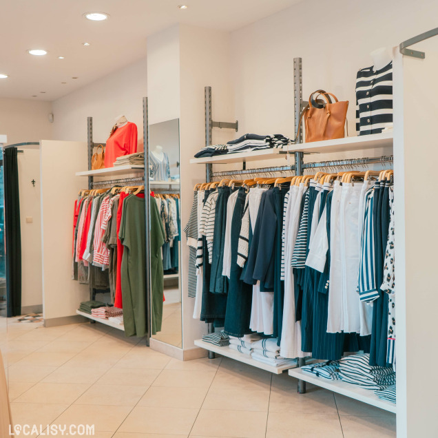 Intérieur lumineux de la Boutique Georgette à Huy, montrant des portants de vêtements variés.