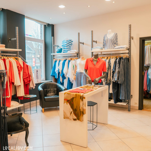 Agencement intérieur de la Boutique Georgette à Huy avec des vêtements exposés et un fauteuil.
