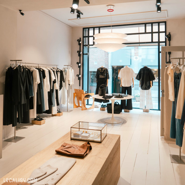 Intérieur du magasin de vêtements Ginette à Liège avec des portants de vêtements et des présentoirs.