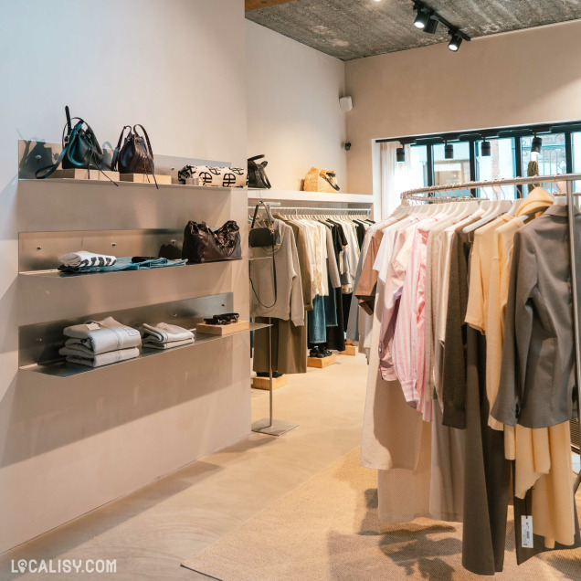 Vue intérieure du magasin de vêtements Ginette à Liège montrant des étagères d'accessoires et des portants.