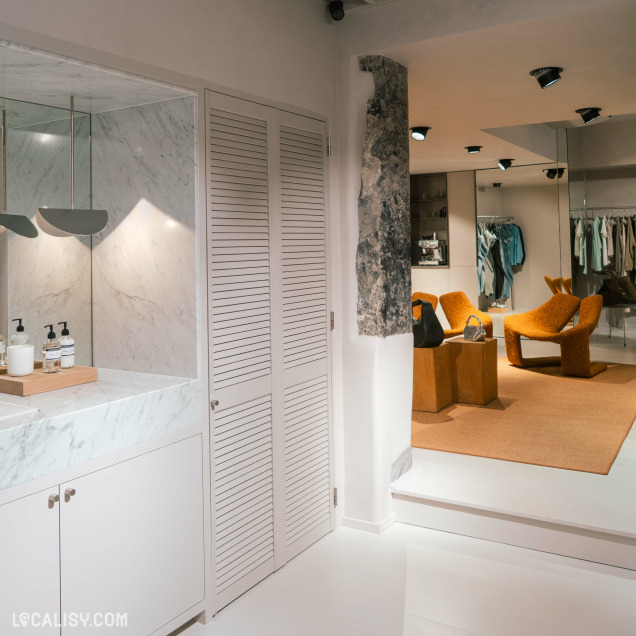 Zone d'essayage ou salle de bain du magasin de vêtements Ginette à Liège avec un lavabo et des portes persiennes.