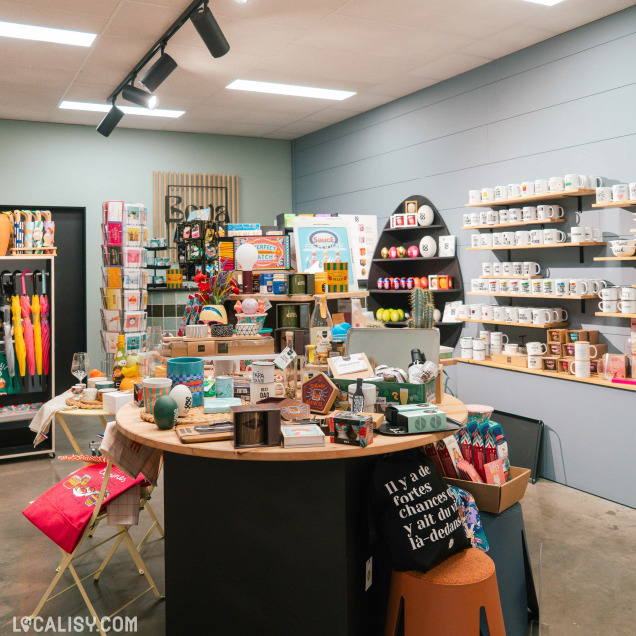 Intérieur du magasin Boya Concept Store à Theux avec une table centrale de produits variés et des tasses sur des étagères.