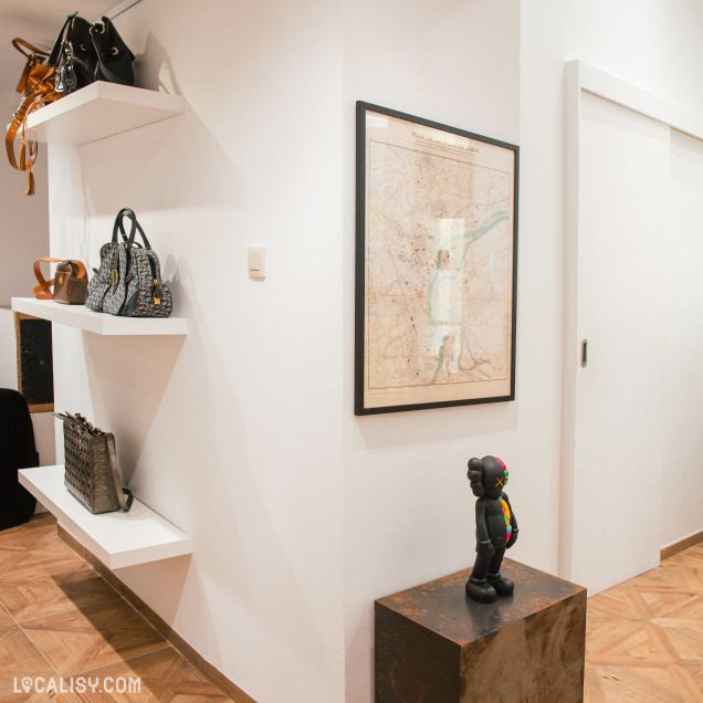Détail de l'intérieur du magasin de dépôt-vente Vingt-Trois Shop à Liège avec un mur décoré et des sacs exposés.