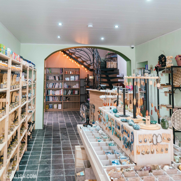 Allée principale de l'herboristerie La Boutique de l'Enchanteresse à Huy, avec des présentoirs de bijoux et un escalier au fond.