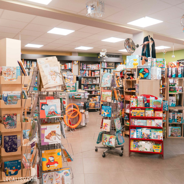 Vue d'ensemble du magasin de jouets La poule aux jeux d'or à Rochefort, avec une employée et divers rayons.